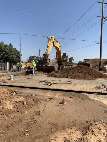 Storm Drain installation in the intersection of McKinley and McCall Avenues. Large Excavator with large bucket pictured alongside several laborers.