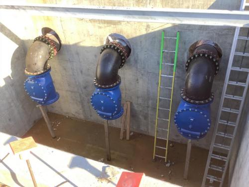 ductile iron pipe elbows with vertically oriented swing check valves pertruding from the concrete wall of the Fancher Creek pump intake structure.