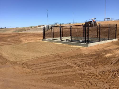 Finished pump intake structure with a 6' tall black vinyl coated chain link fence around its square perimeter inclusive with a double 12' wide swinging gate.